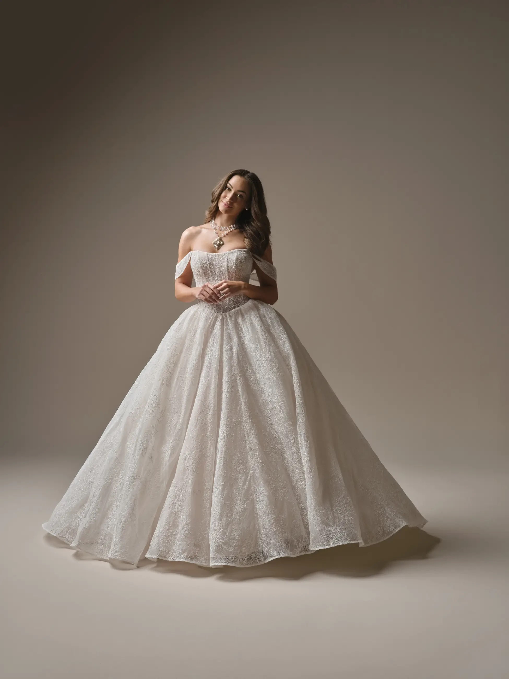 A woman wearing a strapless white wedding dress stands elegantly in a room with brick walls and large windows.
