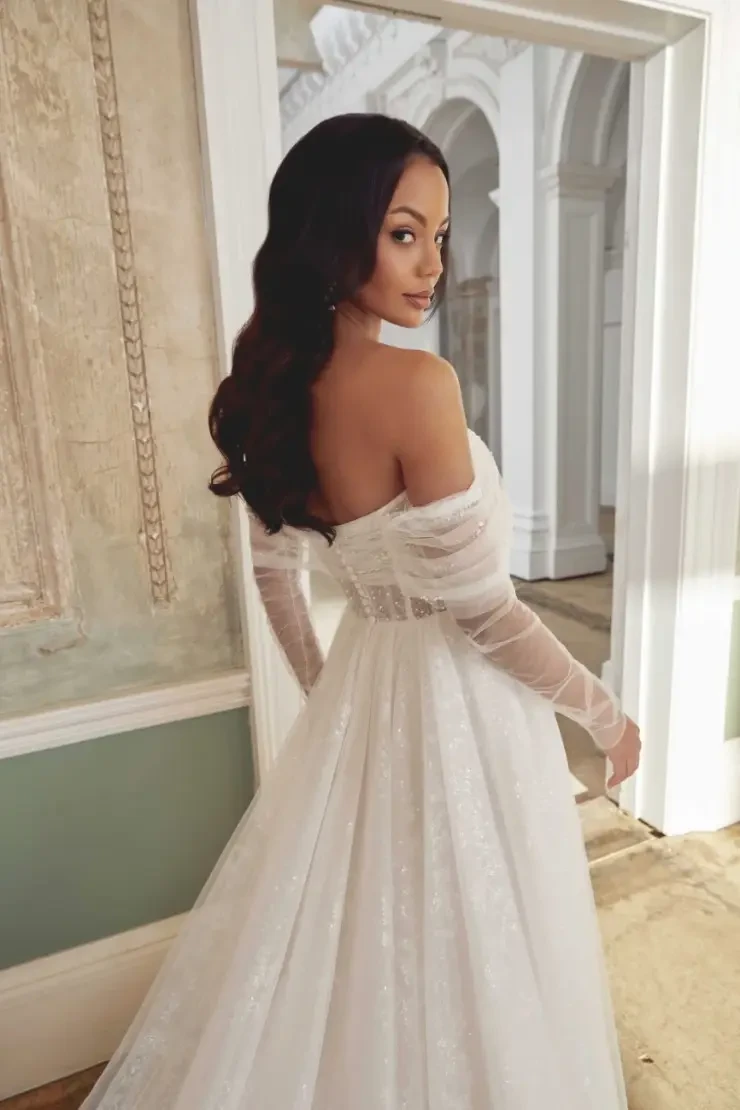 model is wearing an off the shoulder long sleeve wedding gown