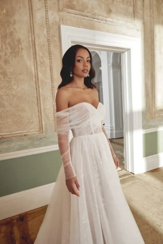 model is wearing an off the shoulder long sleeve wedding gown