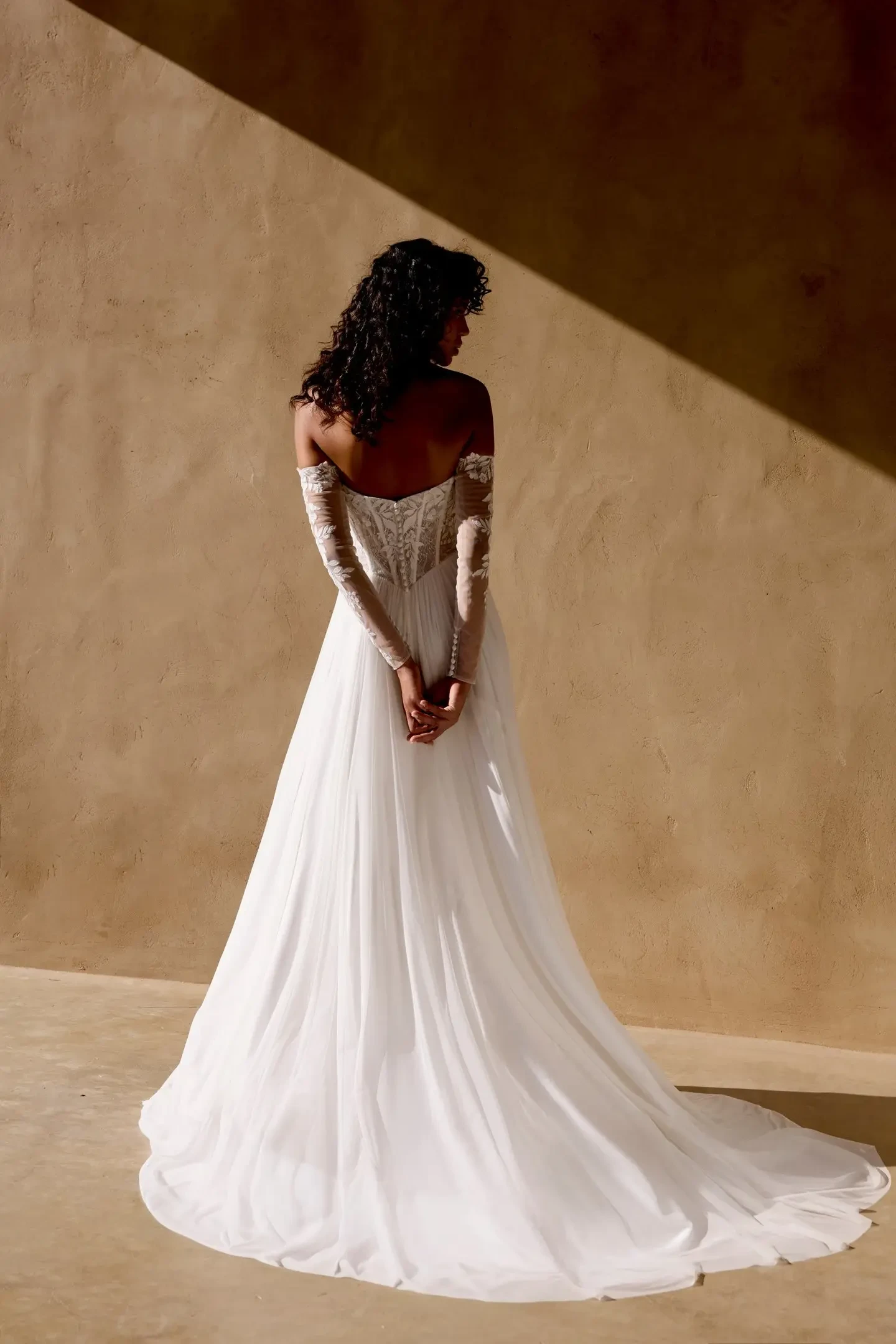 A bride standing with her back to the camera, wearing a strapless white wedding gown with a flowing train.