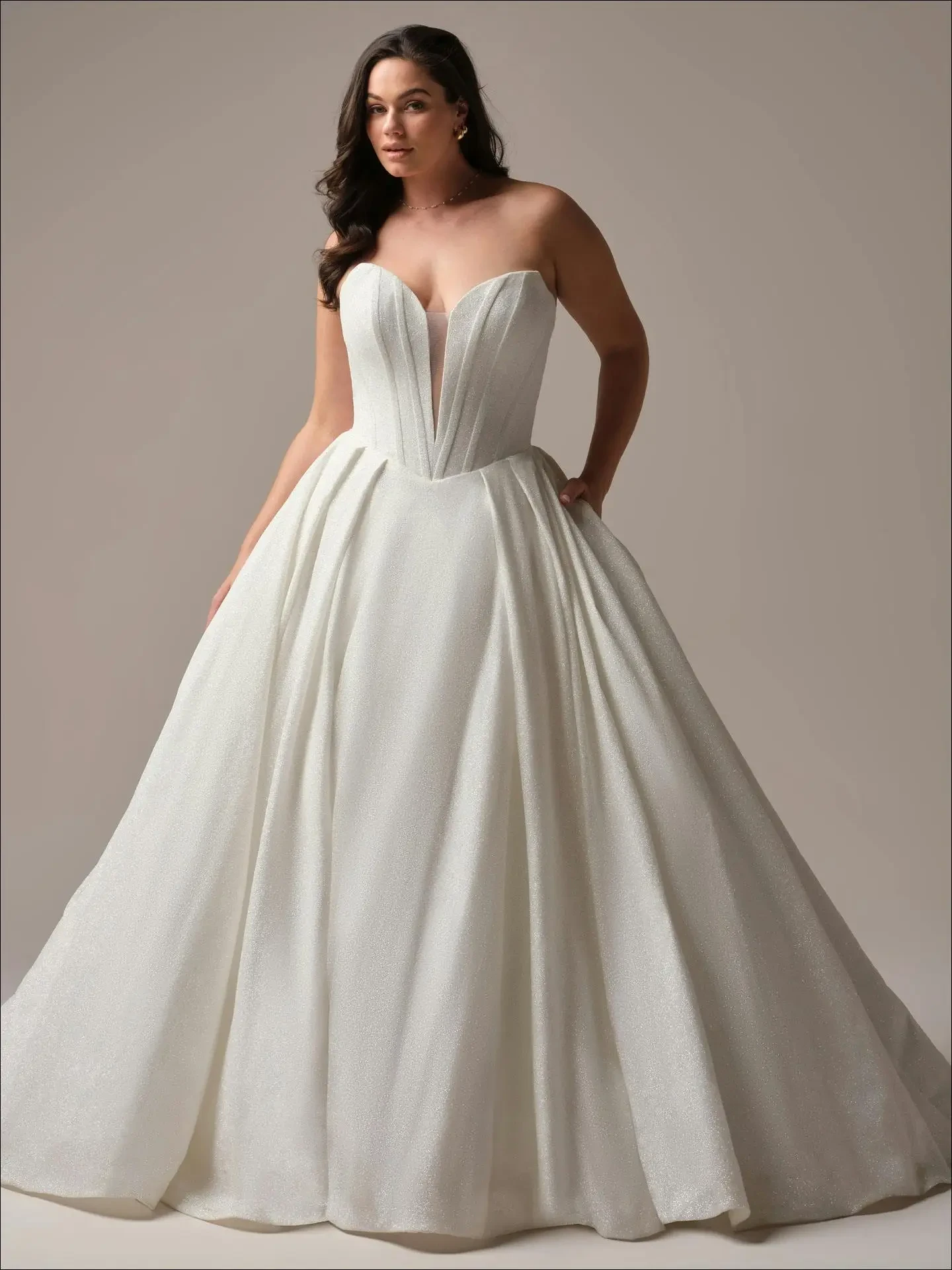 A woman models an elegant, strapless white ball gown with a deep V neckline and full skirt. The dress exudes a classic, sophisticated charm.