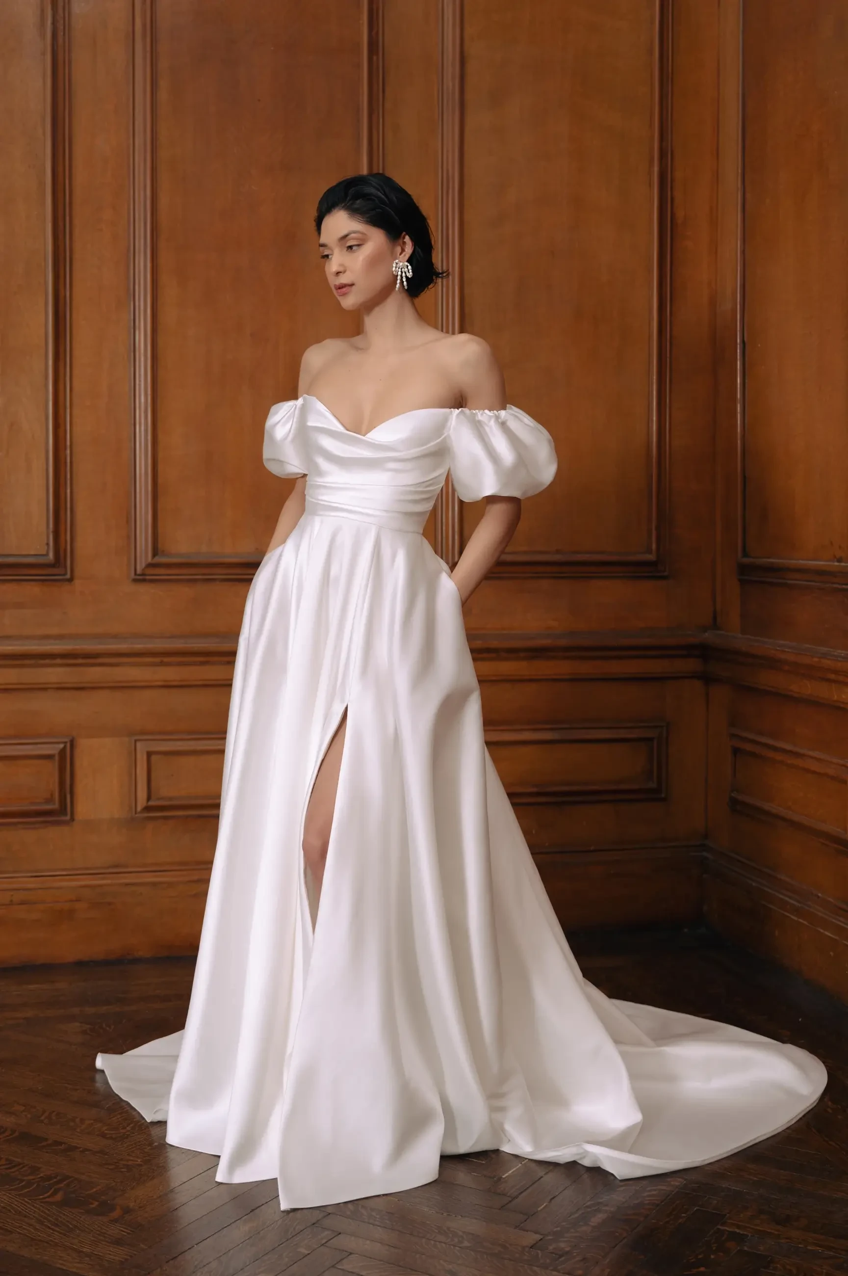 model is wearing an off the shoulder a-line wedding dress with a slit